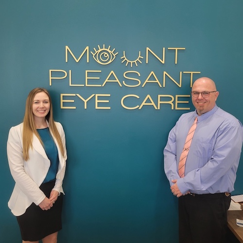 Dr. Katelyn Steen and optician Devin Riley standing either side of the Mount Pleasant Eye Care lettering on the lobby wall